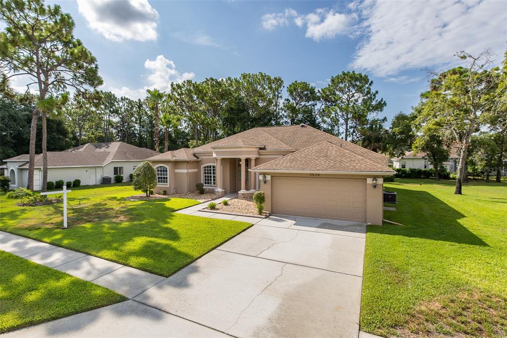 A single-story suburban house with a tan stucco exterior, brown shingle roof, and concrete driveway — 5436 CHAMPIONSHIP CUP LANE, SPRING HILL, FL