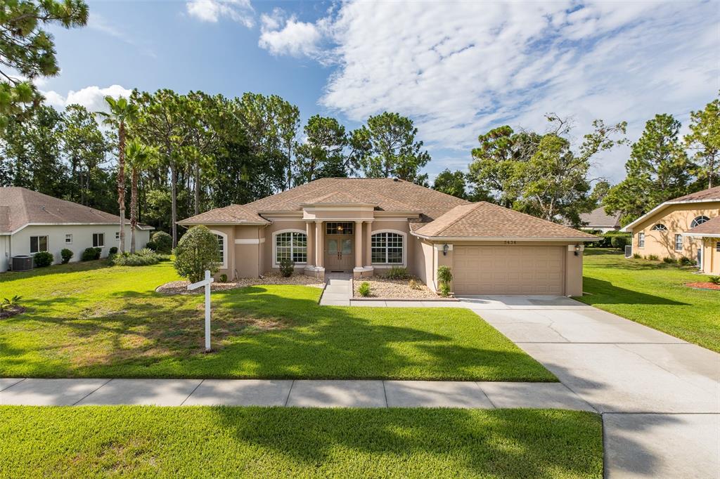 A single-story beige house with a two-car garage and a front lawn under a sky — 5436 CHAMPIONSHIP CUP LANE, SPRING HILL, FL