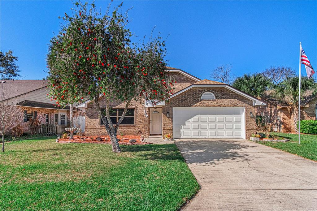 A brick house with a two-car garage, a concrete driveway, and a large flowering tree — 152 LOON COURT, DAYTONA BEACH, FL