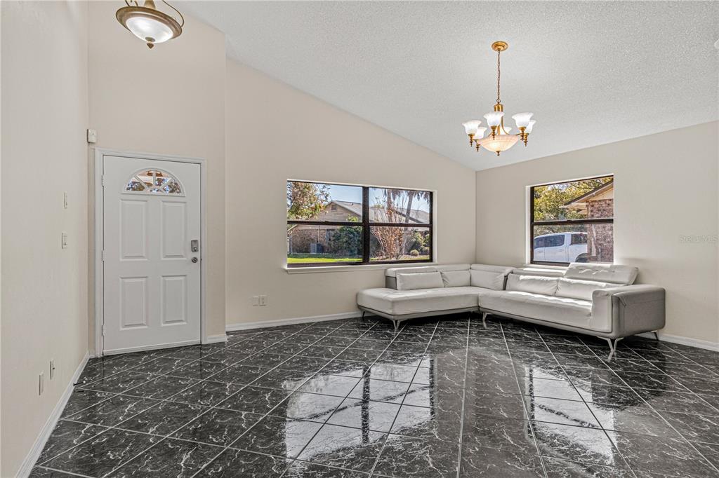 A living room with black marble-style tile flooring, a white sectional sofa, and vaulted ceilings — 152 LOON COURT, DAYTONA BEACH, FL