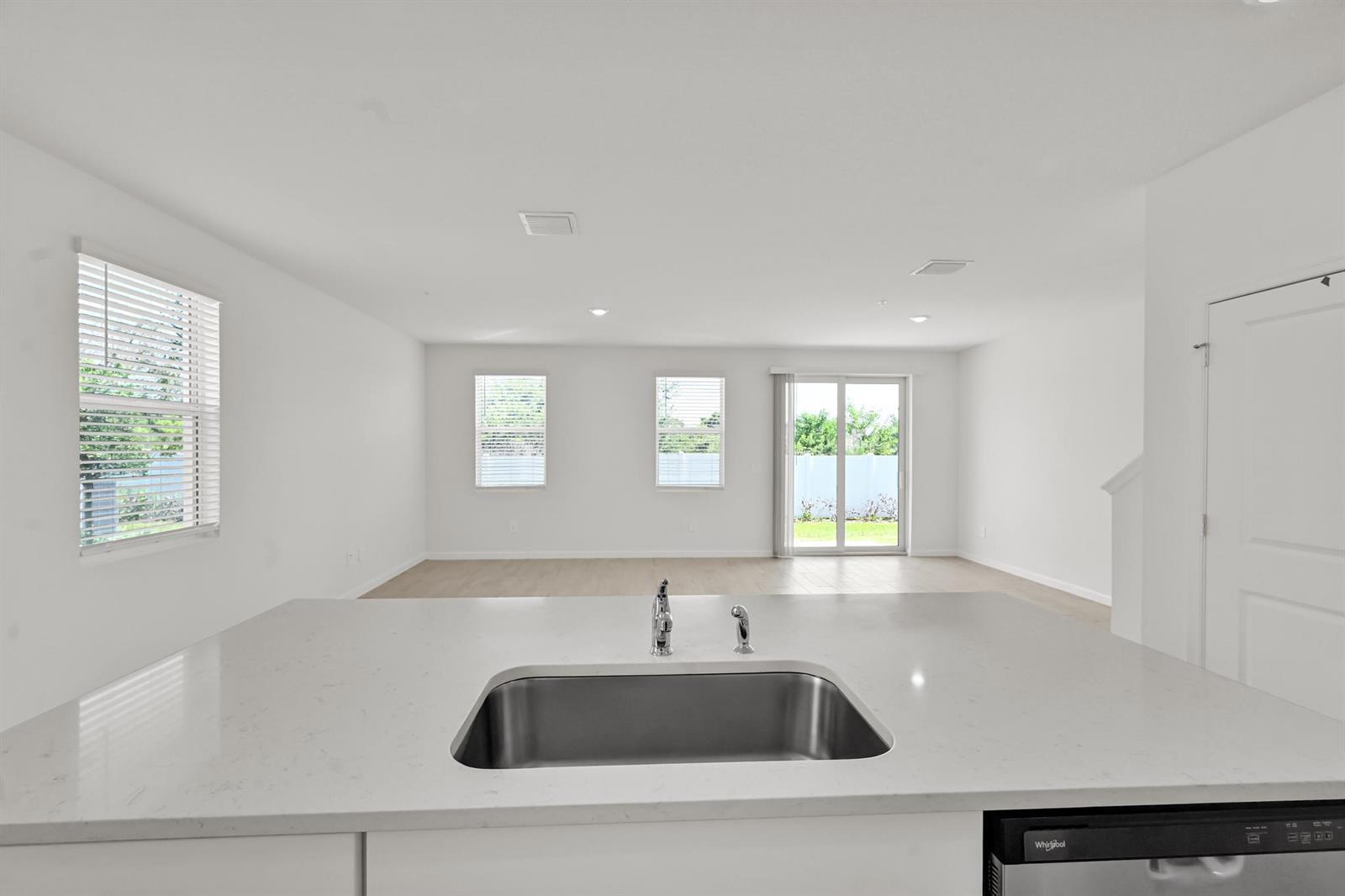 A kitchen island with a stainless steel sink overlooks an open-concept living area with windows — 575 Salisbury Circle, Fort Pierce FL 34982, FORT PIERCE, FL