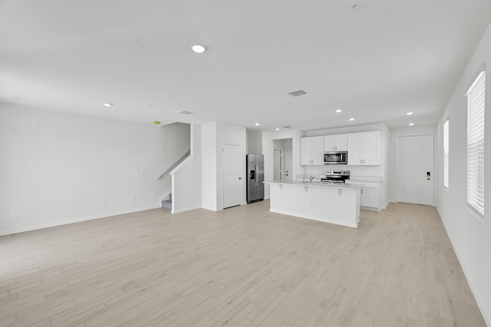 An open-concept living area features light wood-look flooring, white walls, and a modern kitchen — 575 Salisbury Circle, Fort Pierce FL 34982, FORT PIERCE, FL
