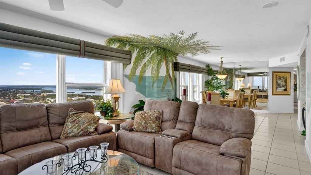 A living room features brown reclining sofas, a palm tree mural, and panoramic water views — 3425 S ATLANTIC AVENUE UNIT 1706, DAYTONA BEACH, FL