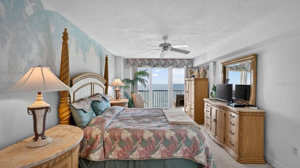 A bedroom features a four-poster bed, floral bedding, a dresser with a mirror, and ocean views — 3425 S ATLANTIC AVENUE UNIT 1706, DAYTONA BEACH, FL