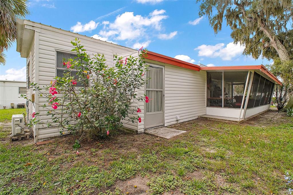 A white mobile home exterior features a flowering hibiscus bush and a screened-in porch — 11723 MAGNOLIA AVENUE, TAVARES, FL