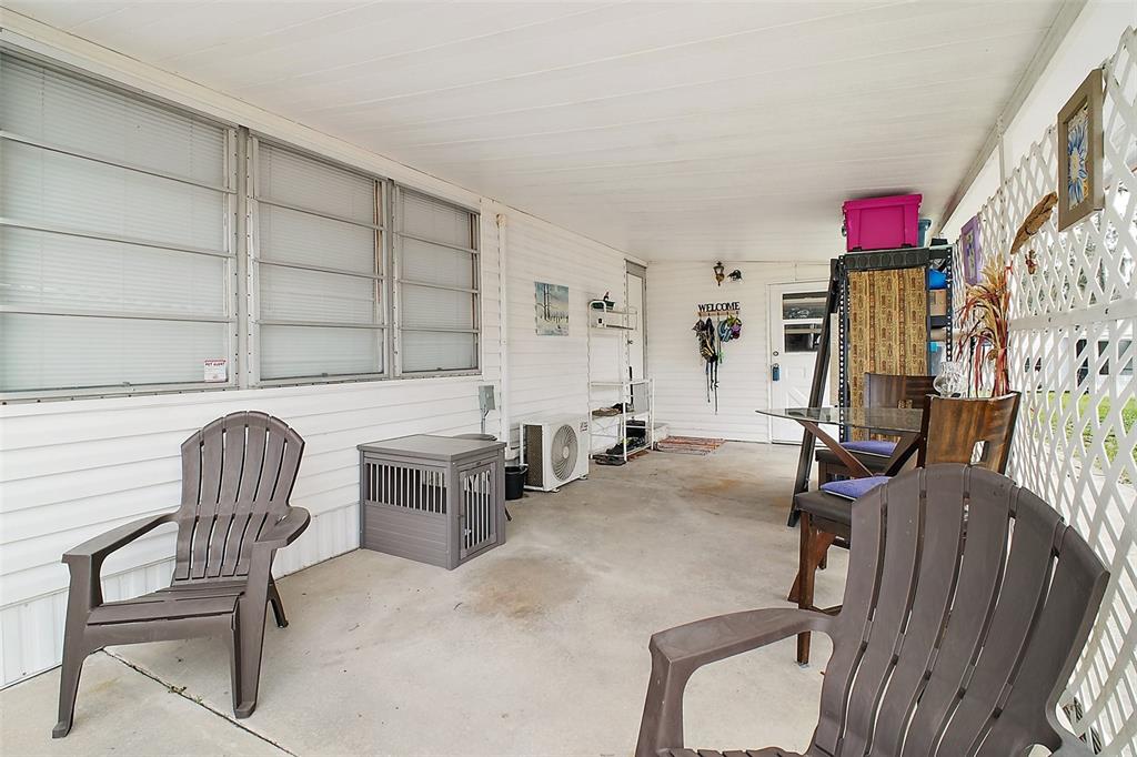 A covered outdoor patio with concrete flooring, white siding, and two brown plastic chairs — 11723 MAGNOLIA AVENUE, TAVARES, FL