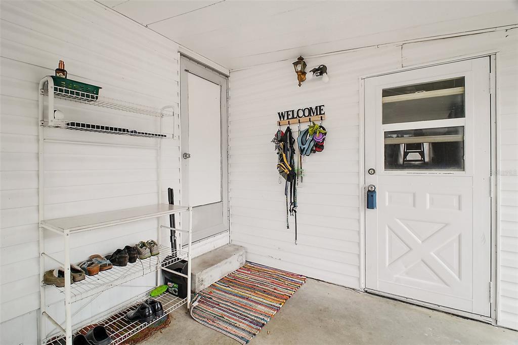 A covered porch features a white door, a shoe rack, and a welcome sign — 11723 MAGNOLIA AVENUE, TAVARES, FL