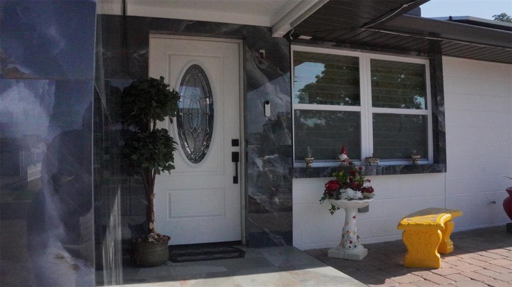 A white front door with an oval glass insert sits beside a window and bench — 4527 W ELM STREET, TAMPA, FL