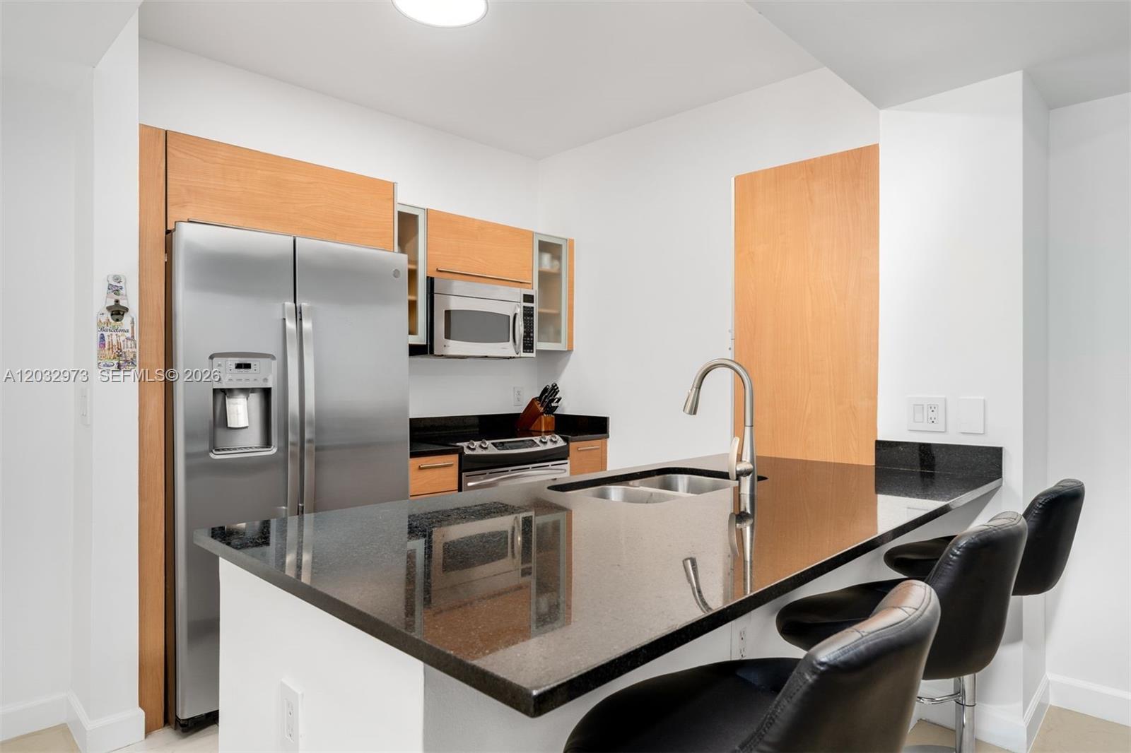 A kitchen features a black granite island, stainless steel appliances, and light wood cabinetry — 950 Brickell Bay Dr # 803, Miami FL 33131, MIAMI, FL