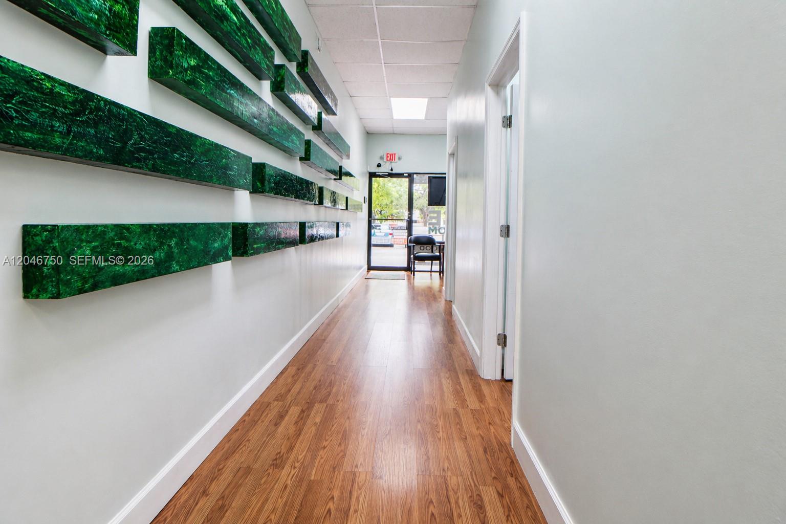 A hallway features wood-look flooring, light walls, and a wall display of green rectangular blocks — HALLANDALE BEACH, FL