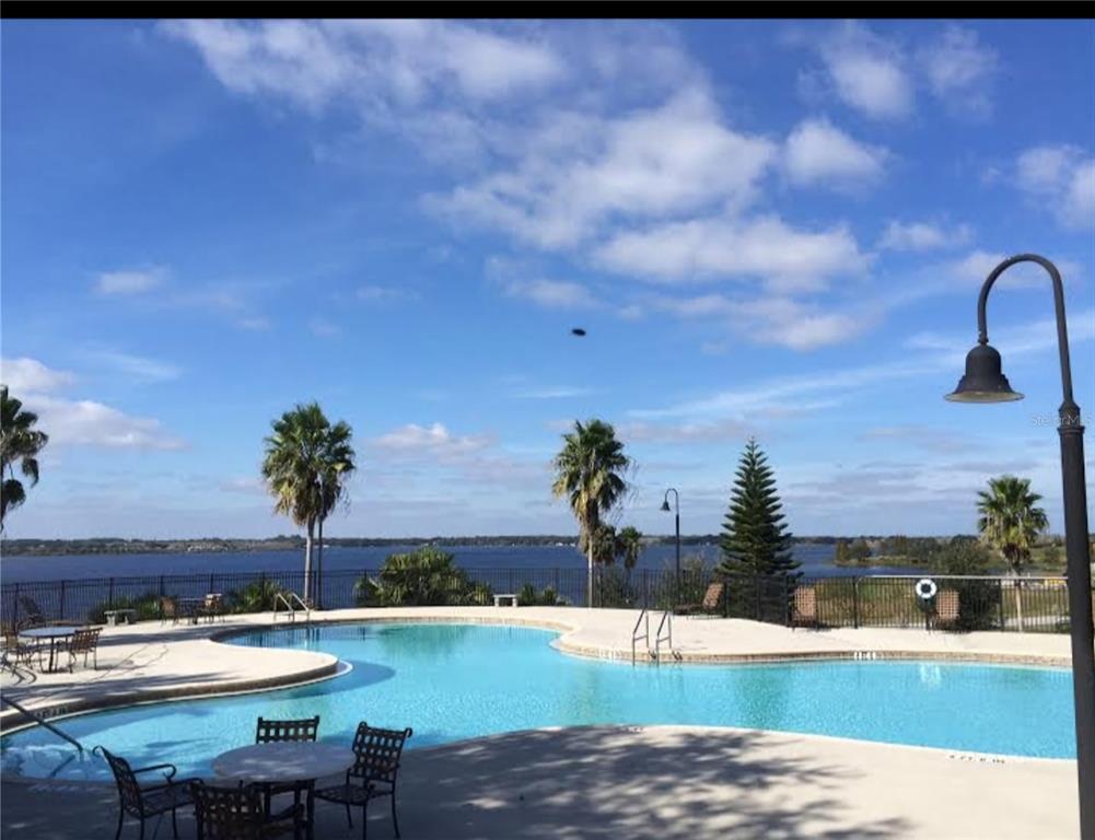 A swimming pool overlooks a large lake under a blue sky with scattered clouds — 780 WATERFERN TRAIL DRIVE, AUBURNDALE, FL