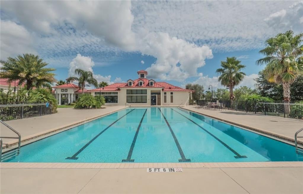 A rectangular swimming pool with lap lanes sits in front of a community clubhouse building — 780 WATERFERN TRAIL DRIVE, AUBURNDALE, FL
