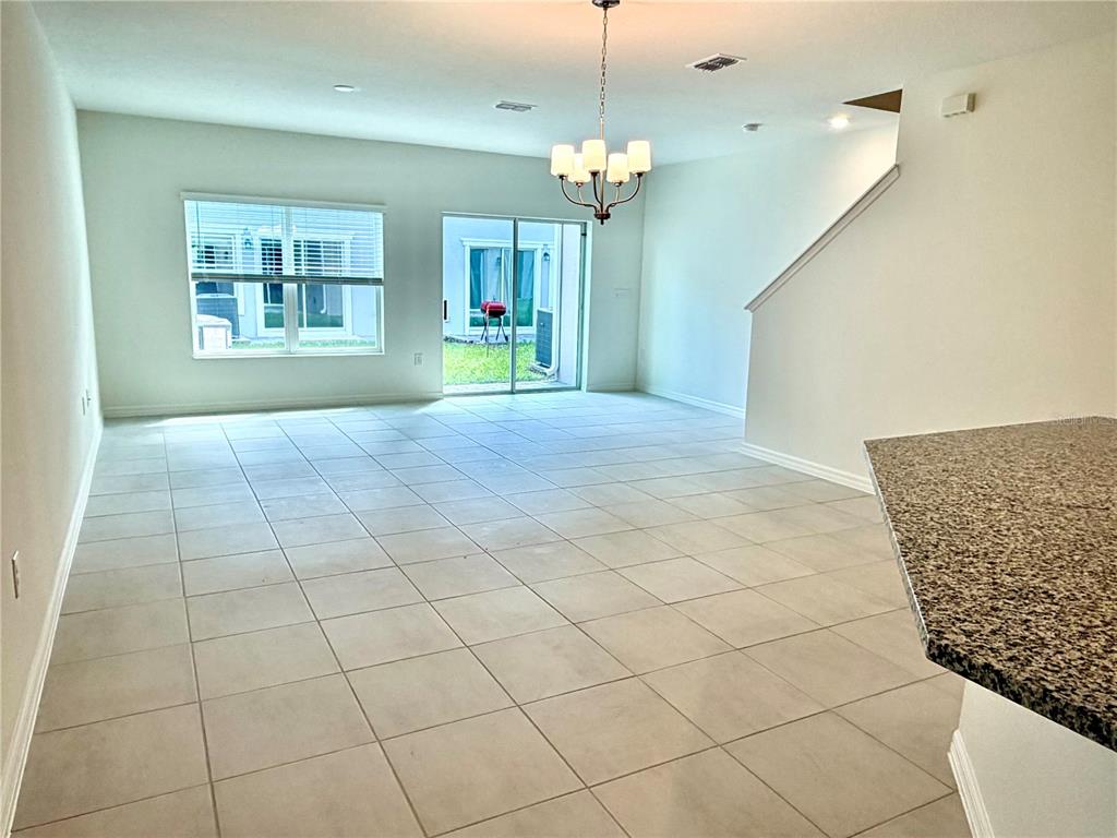 An open-concept living area features light tile flooring, a dining chandelier, and sliding glass doors — 2817 MOONSHADOW COURT, CLERMONT, FL