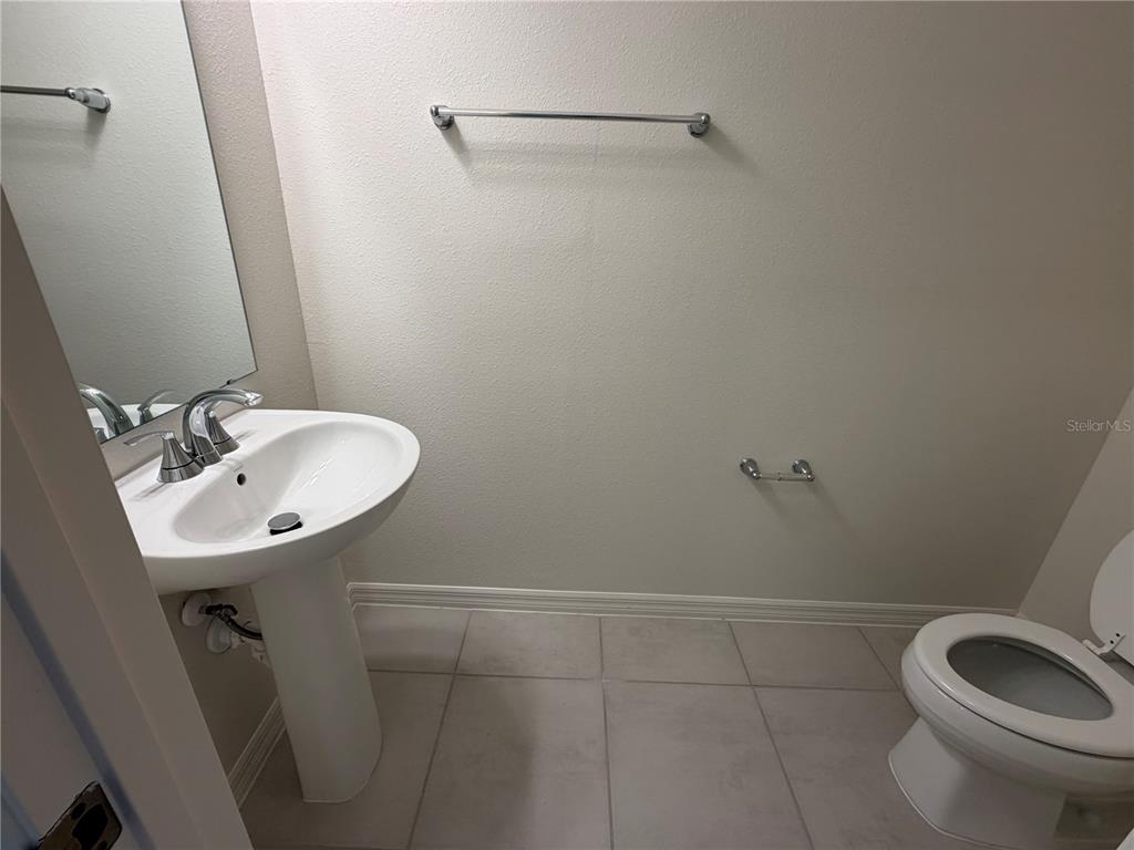A small bathroom features a pedestal sink, a toilet, and a wall-mounted towel bar — 2817 MOONSHADOW COURT, CLERMONT, FL