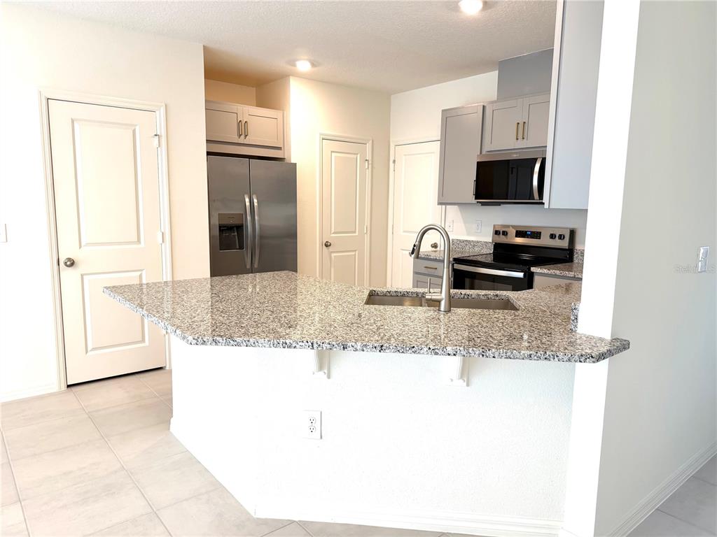 A kitchen with granite countertops, stainless steel appliances, and gray cabinets — 2817 MOONSHADOW COURT, CLERMONT, FL