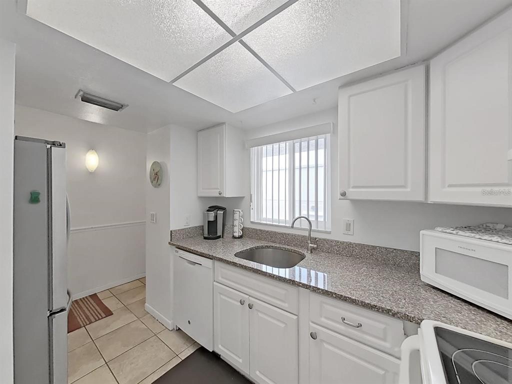 A kitchen features white cabinets, granite countertops, a stainless steel sink, and tile flooring — 215 VALENCIA BOULEVARD UNIT 213, LARGO, FL