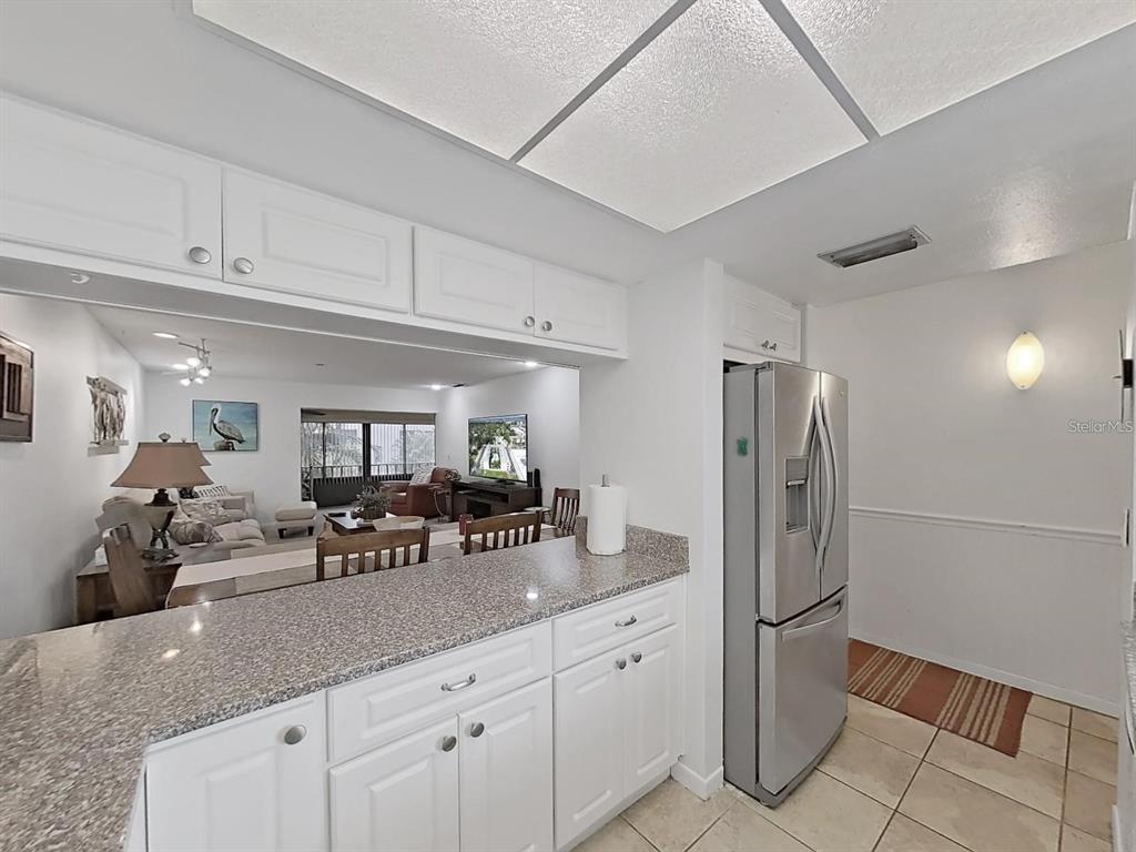 A kitchen with white cabinets and granite countertops overlooks a living room with tile flooring — 215 VALENCIA BOULEVARD UNIT 213, LARGO, FL