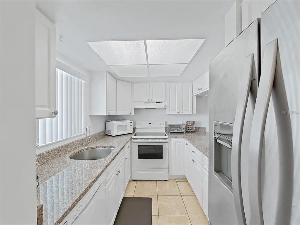A galley kitchen features white cabinets, granite countertops, stainless steel appliances, and tile flooring — 215 VALENCIA BOULEVARD UNIT 213, LARGO, FL