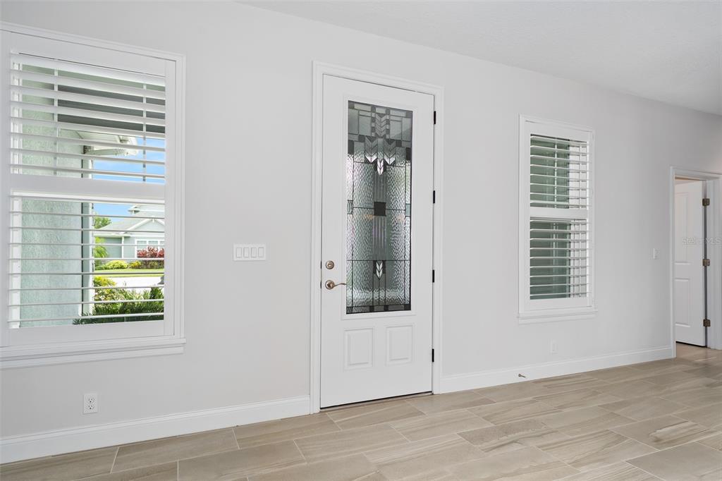 A bright entryway features a white front door with decorative glass, plantation shutters, and tile flooring — 3322 MODENA WAY, NEW SMYRNA BEACH, FL