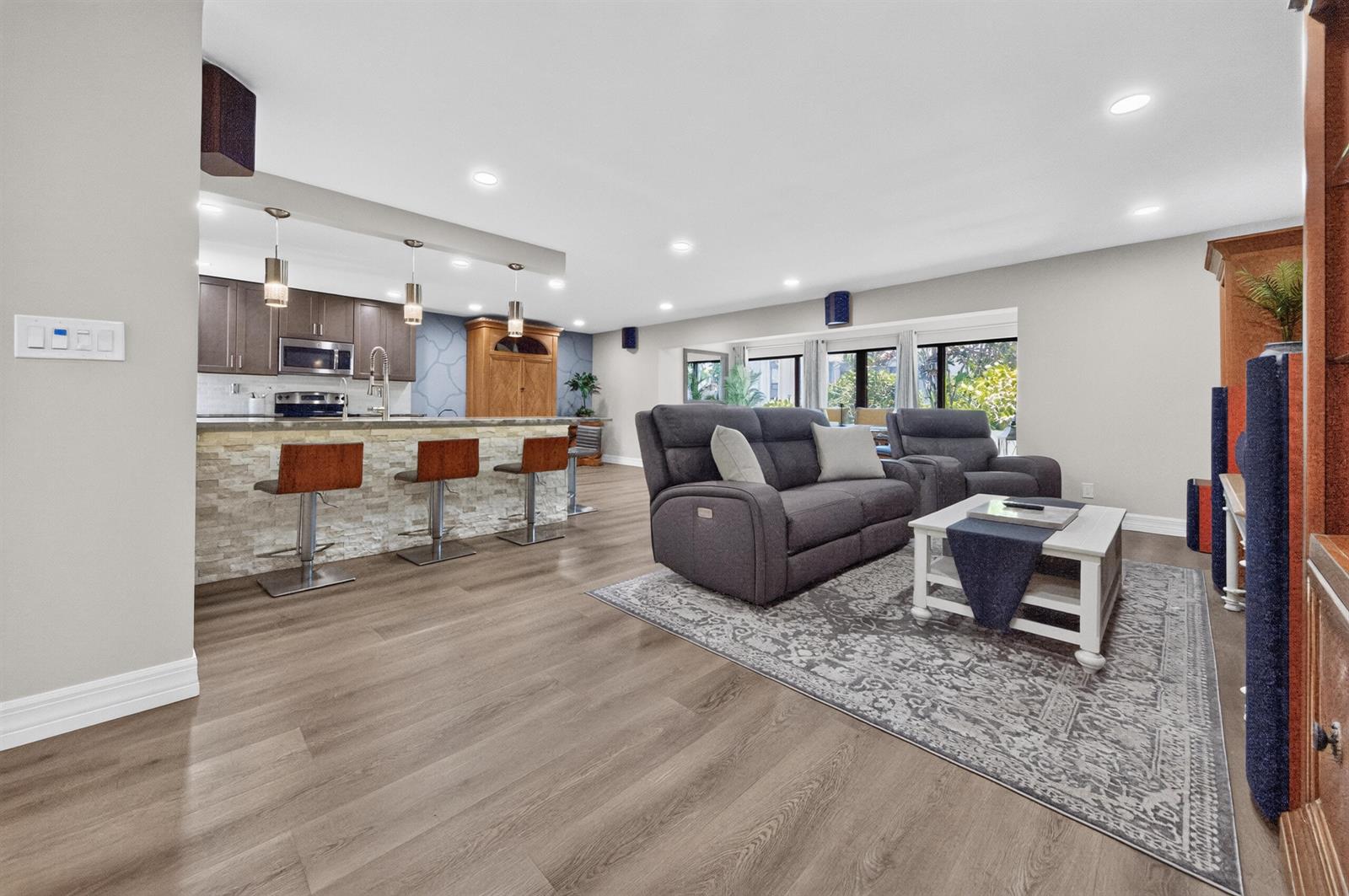 An open-concept living room and kitchen featuring wood-look flooring, a stone-faced breakfast bar, and gray furniture — 6593 Spring Bottom Way # 137, Boca Raton FL 33433, BOCA RATON, FL