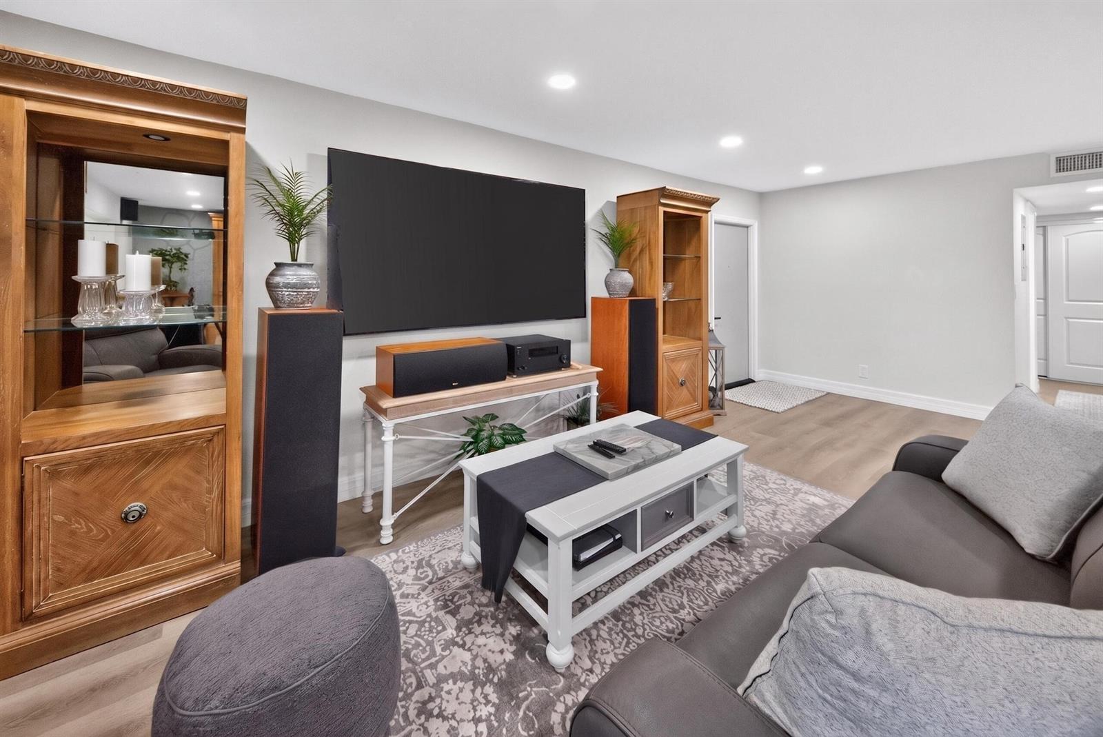 A living room features a large wall-mounted television, wooden shelving units, and a grey sofa — 6593 Spring Bottom Way # 137, Boca Raton FL 33433, BOCA RATON, FL
