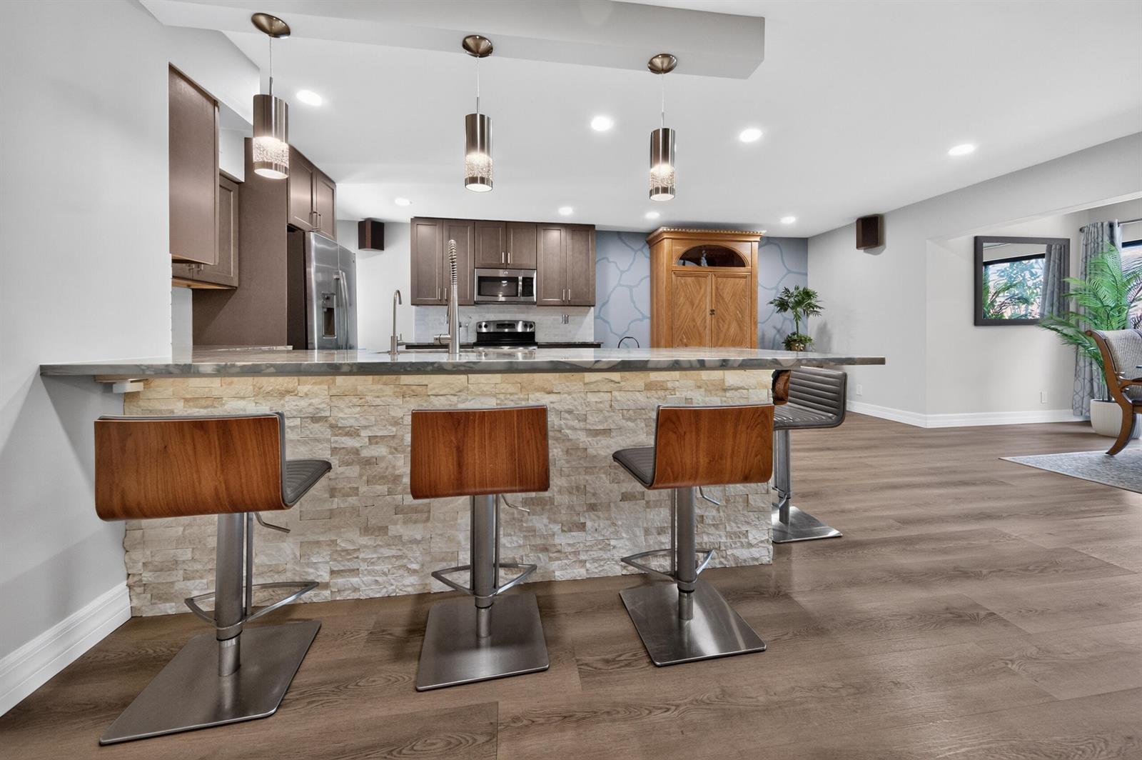 A kitchen features a stone-faced island with bar stools, dark cabinetry, and pendant lighting — 6593 Spring Bottom Way # 137, Boca Raton FL 33433, BOCA RATON, FL