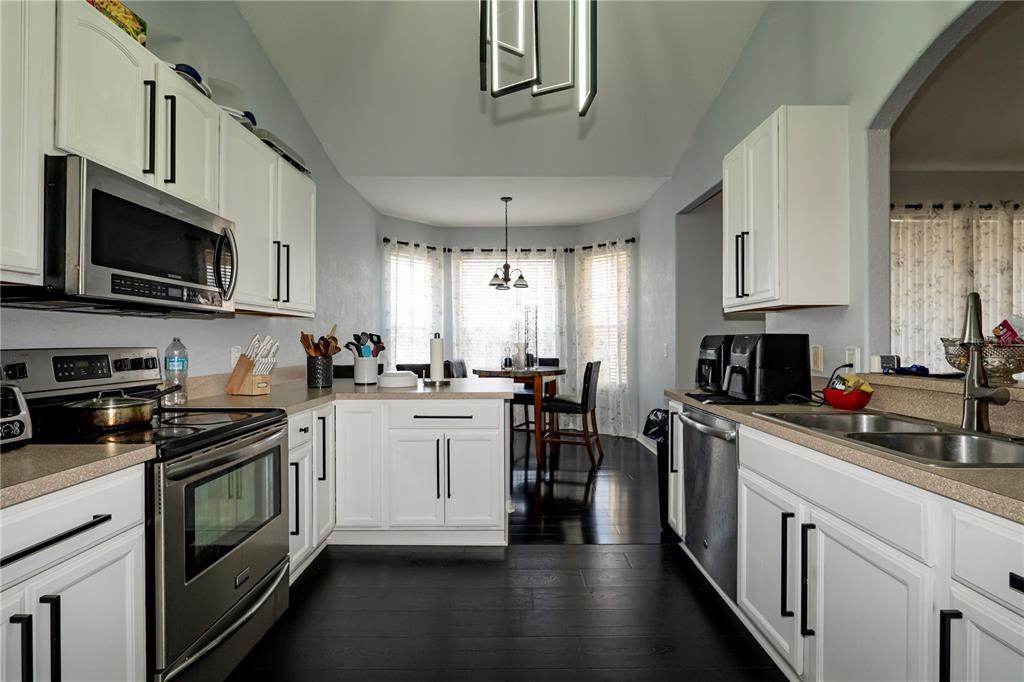 A kitchen with white cabinets, stainless steel appliances, and dark wood floors leads to a dining area — 276 TERRANOVA BOULEVARD, WINTER HAVEN, FL