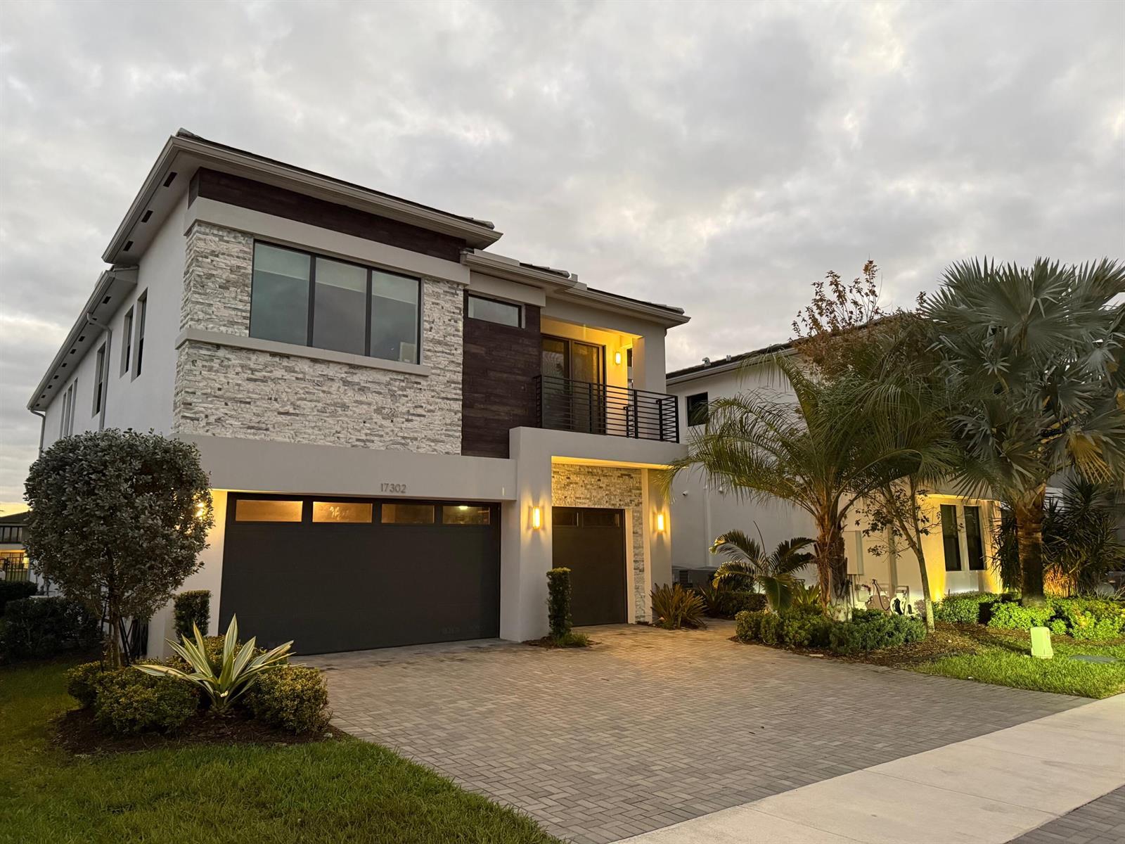 A two-story modern house features a stone facade, dark wood accents, and a paved driveway — 17302 Rainstream Road, Boca Raton FL 33496, BOCA RATON, FL