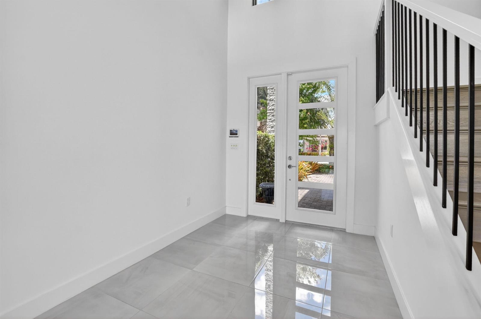 A bright entryway features white walls, large gray floor tiles, and a modern glass-paneled door — 17302 Rainstream Road, Boca Raton FL 33496, BOCA RATON, FL