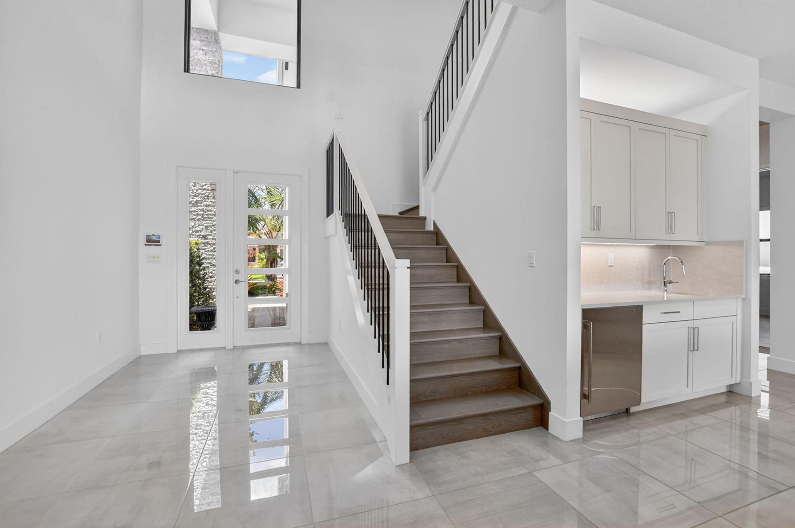 A bright entryway features a staircase with wooden treads, white walls, and tiled flooring — 17302 Rainstream Road, Boca Raton FL 33496, BOCA RATON, FL