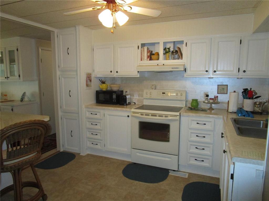 A covered patio with gray siding, a white door, and large windows with vertical blinds — 47 KONO CIRCLE, LEESBURG, FL