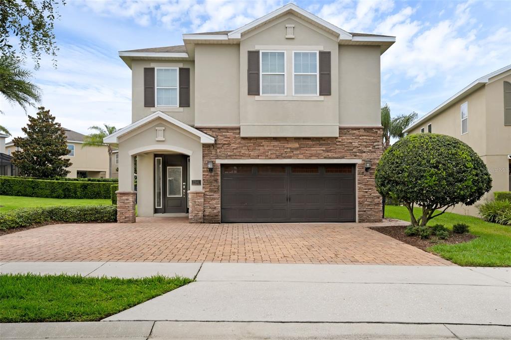 A two-story house with a stone-accented facade, a two-car garage, and a brick paver driveway — 7541 MARKER AVENUE, KISSIMMEE, FL