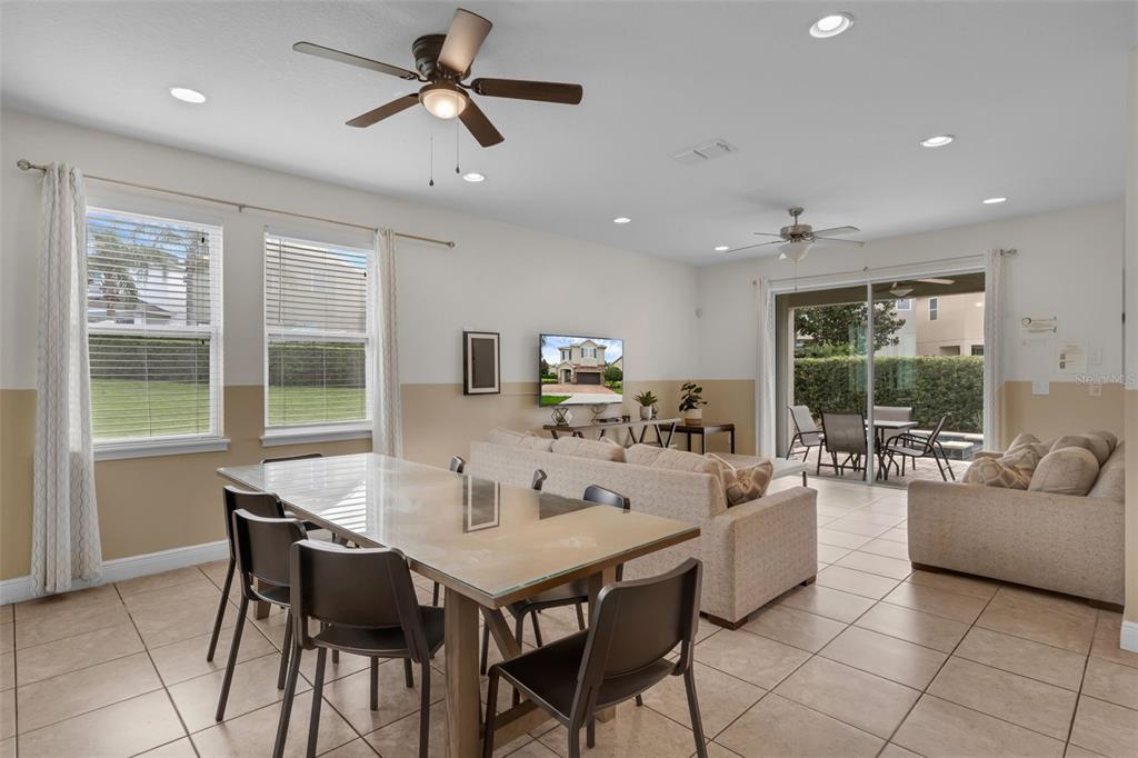 An open-concept living and dining area features tile flooring, a glass-top table, and sliding doors — 7541 MARKER AVENUE, KISSIMMEE, FL