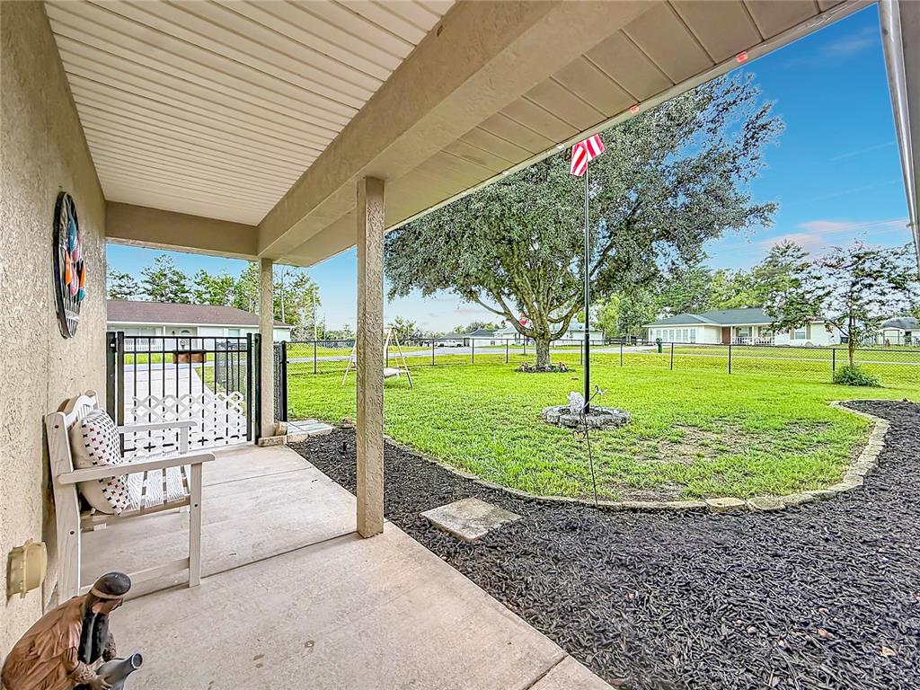 A covered concrete porch overlooks a grassy backyard with a large tree and metal fence — 1 REDWOOD RUN COURT, OCALA, FL