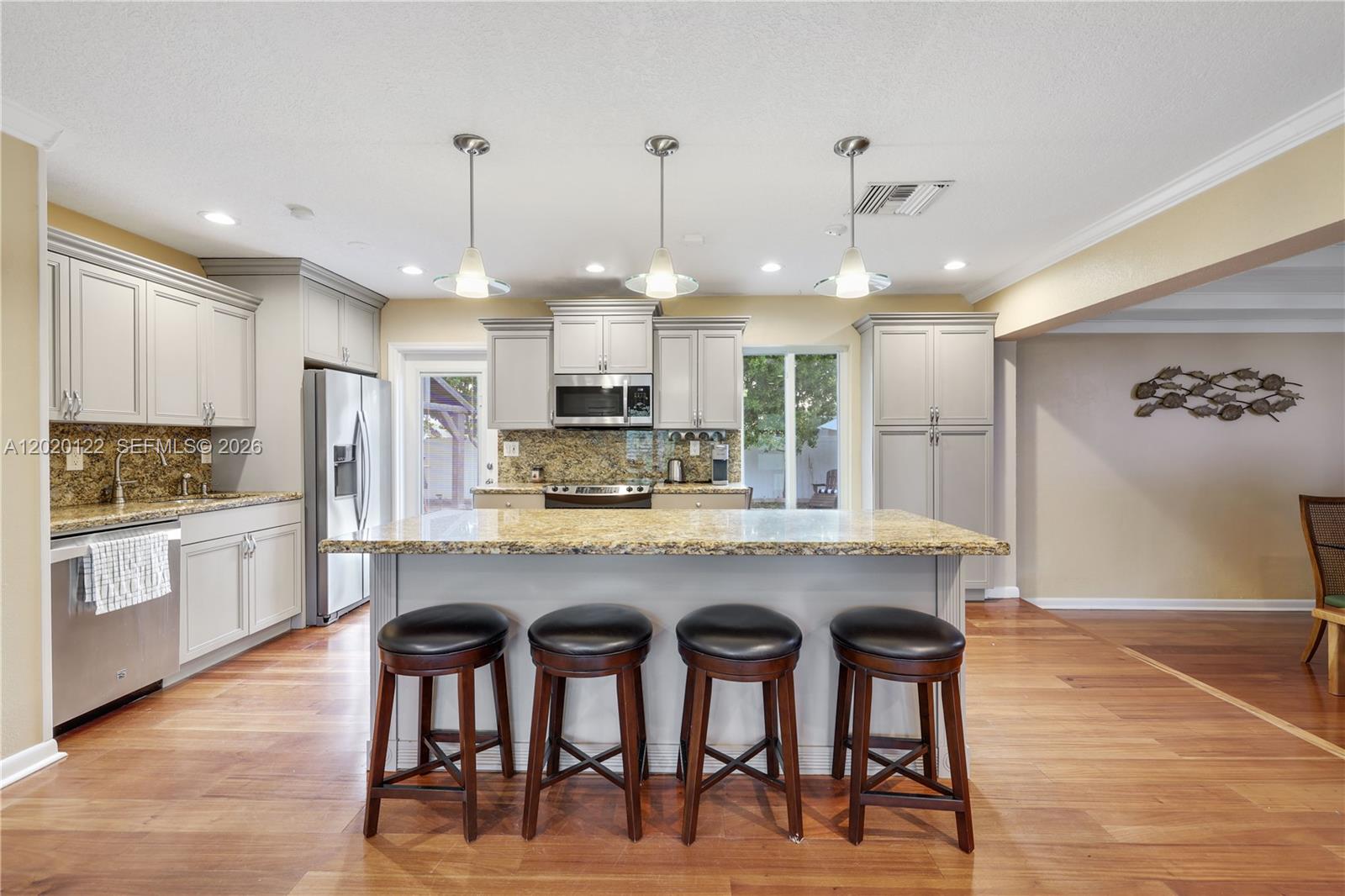 A kitchen features light gray cabinets, granite countertops, a central island, and wood flooring — 1311 NE 26th Ter, Pompano Beach FL 33062, POMPANO BEACH, FL