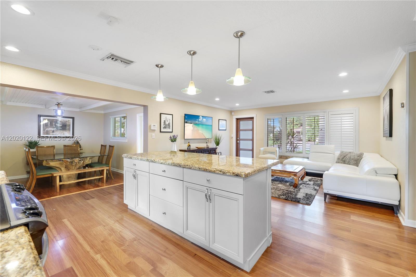 An open-concept kitchen and living area features a granite-topped island and hardwood flooring — 1311 NE 26th Ter, Pompano Beach FL 33062, POMPANO BEACH, FL