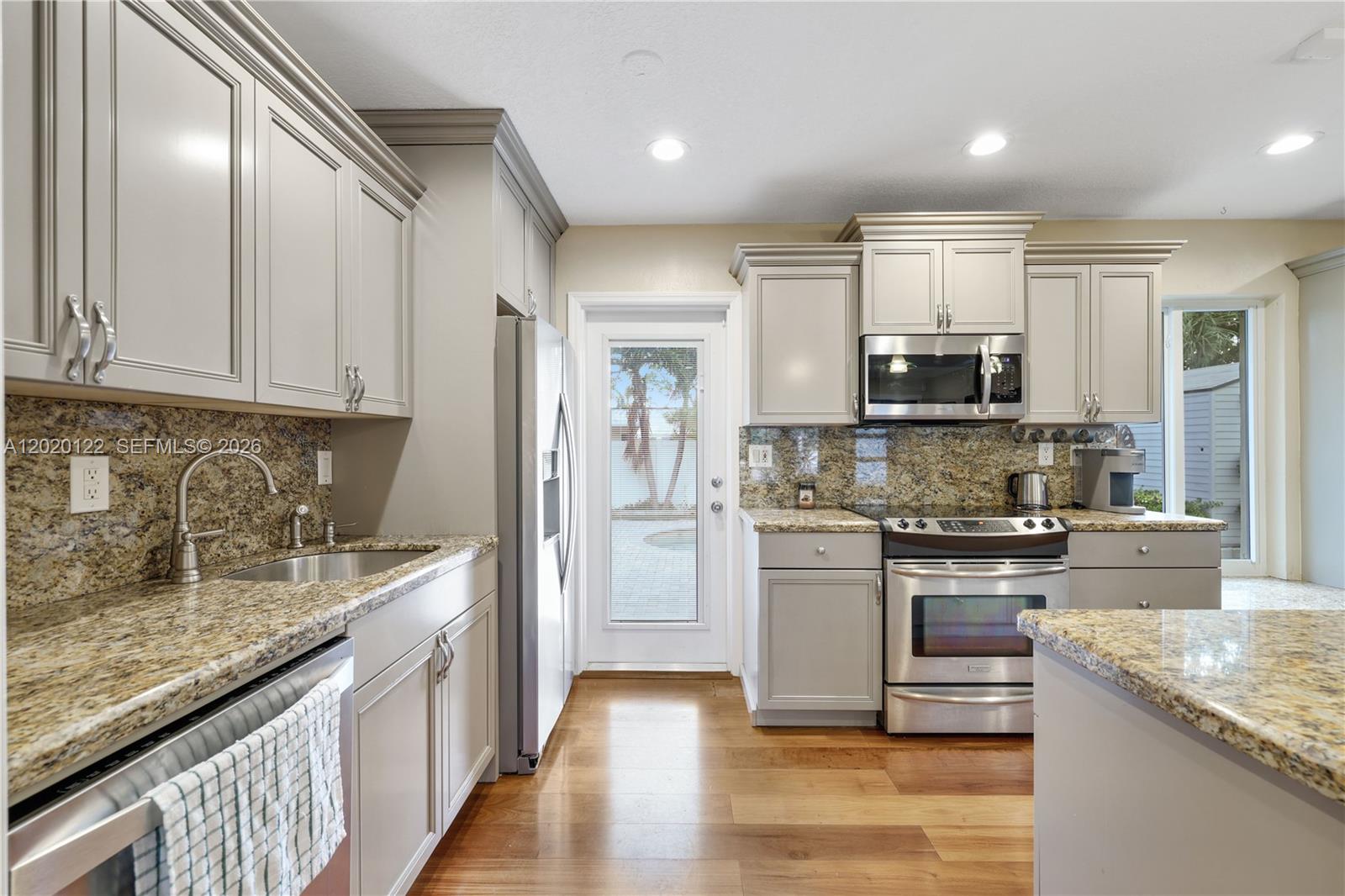 A kitchen features light gray cabinets, granite countertops, stainless steel appliances, and wood flooring — 1311 NE 26th Ter, Pompano Beach FL 33062, POMPANO BEACH, FL