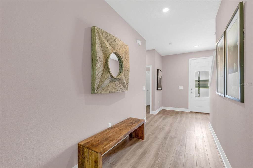 A hallway with light wood flooring, a wooden bench, and wall art leads to a front door — 2729 SANCTUARY DRIVE, CLERMONT, FL