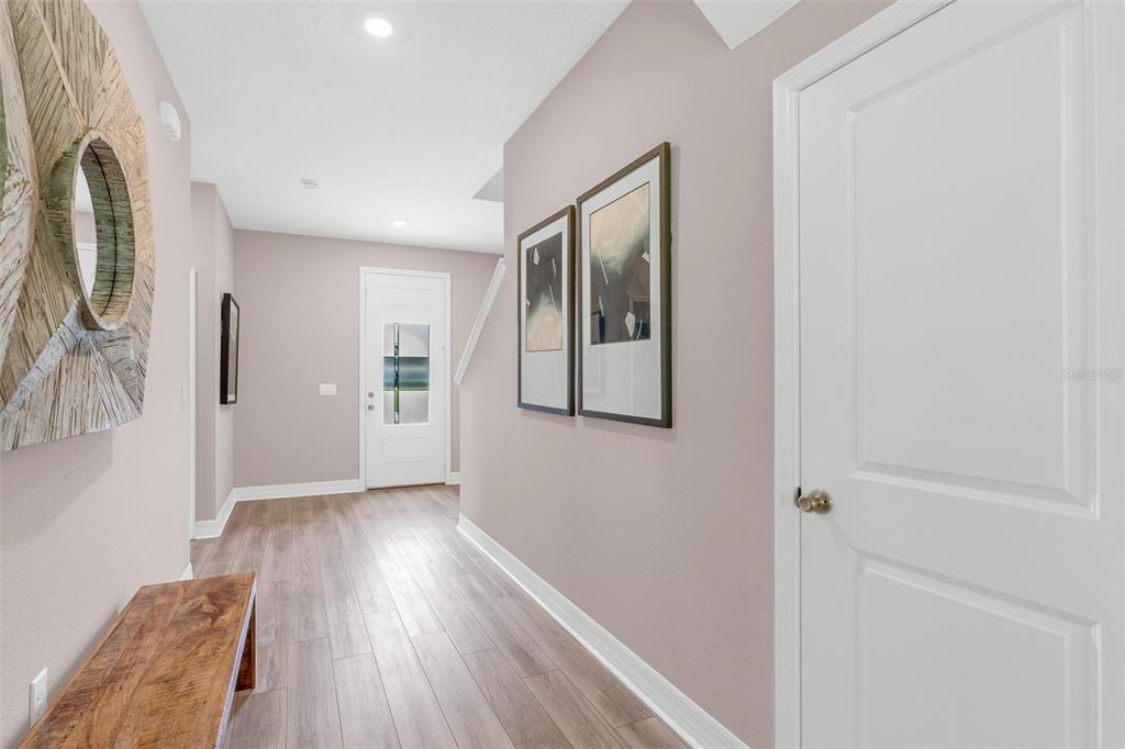 A hallway with light wood-look flooring, a wooden bench, and two framed wall pictures — 2729 SANCTUARY DRIVE, CLERMONT, FL