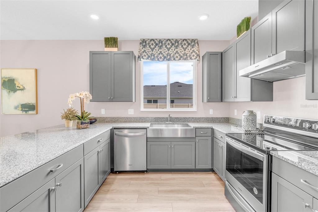 A kitchen features gray cabinets, granite countertops, stainless steel appliances, and a farmhouse sink — 2729 SANCTUARY DRIVE, CLERMONT, FL