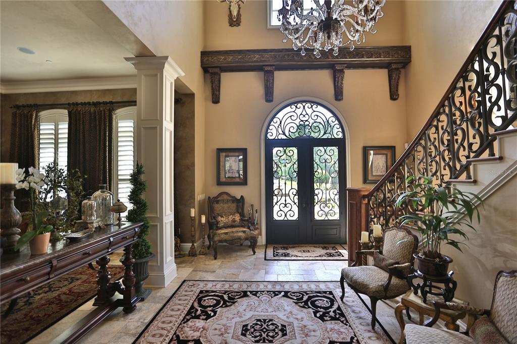 A grand foyer features a stone floor, ornate staircase, double front doors, and a crystal chandelier — 15305 NW HWY 320, MICANOPY, FL