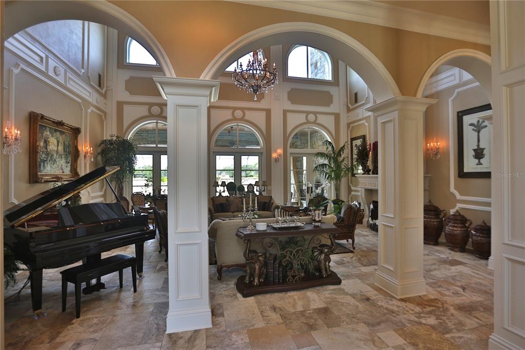 A grand living room features arched entryways, a black grand piano, and stone tile flooring — 15305 NW HWY 320, MICANOPY, FL