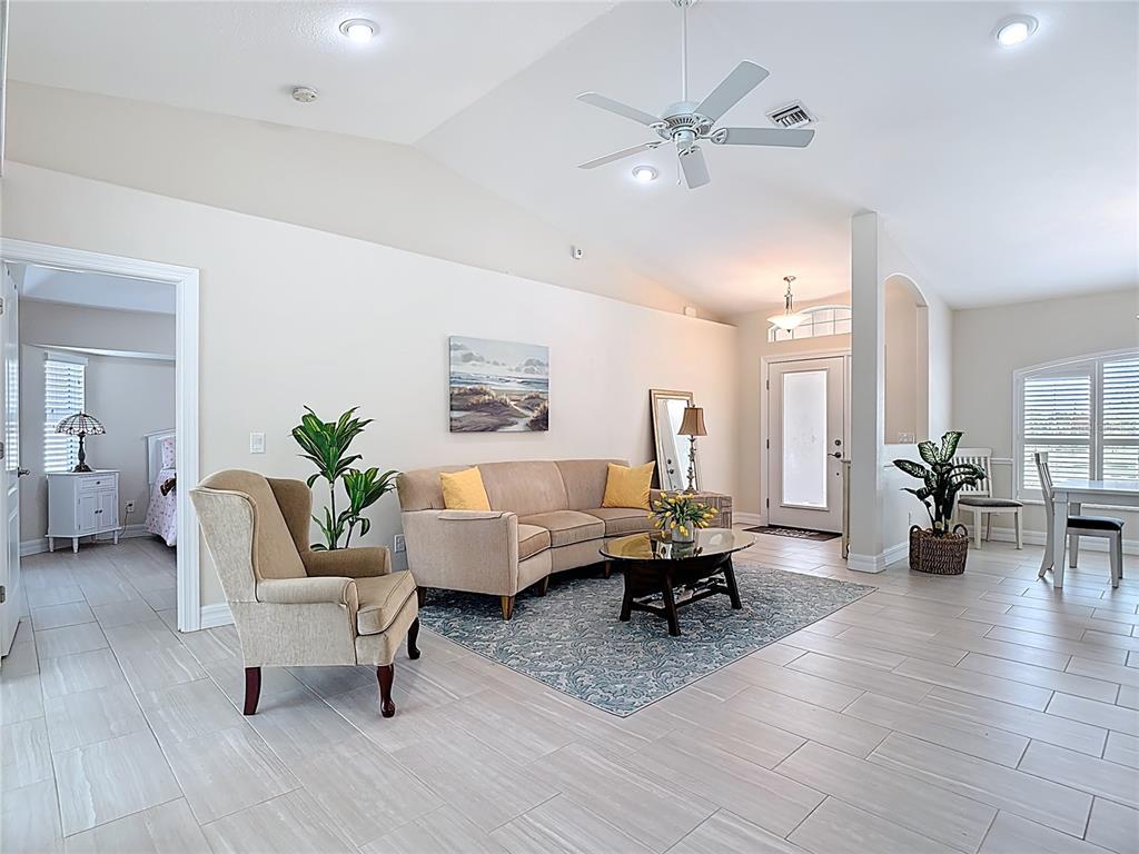 A living room with light tile floors, a vaulted ceiling, and a beige sofa — 70 CLUBHOUSE ROAD, ROTONDA WEST, FL