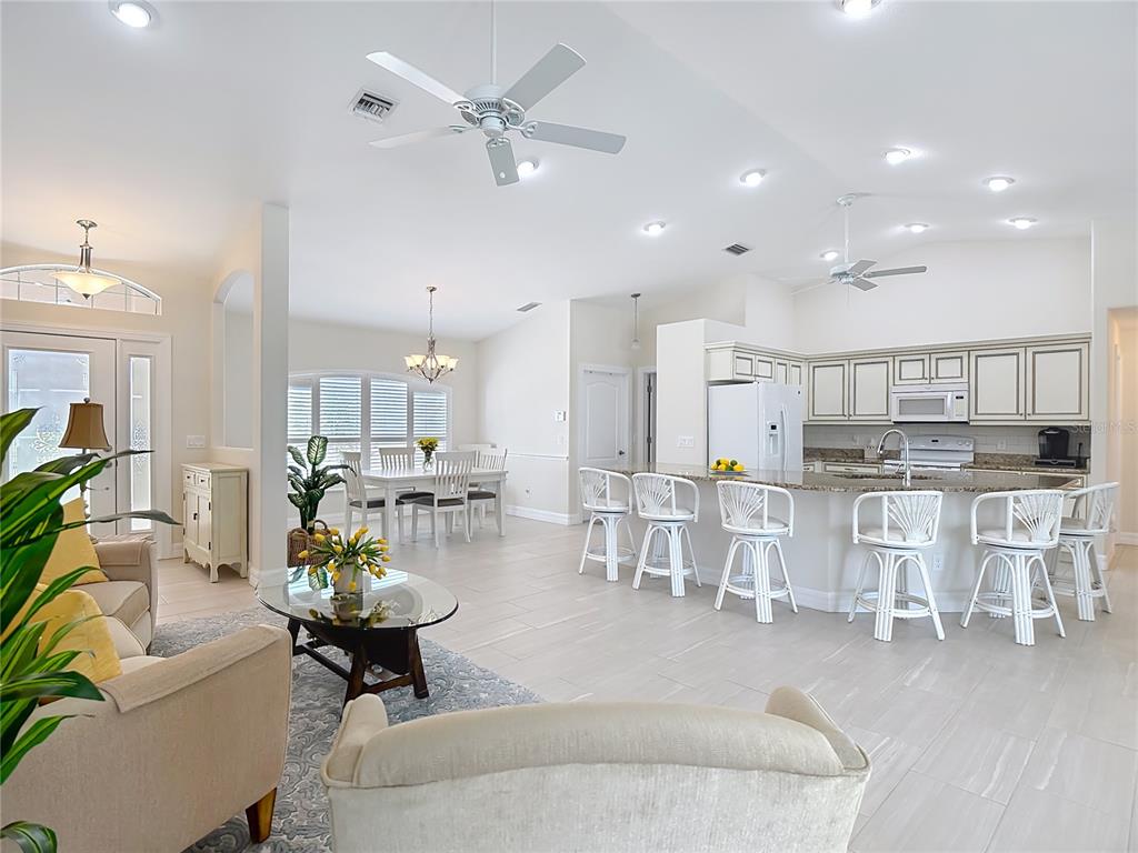 An open-concept living room and kitchen featuring tile floors, white cabinetry, and bar seating — 70 CLUBHOUSE ROAD, ROTONDA WEST, FL