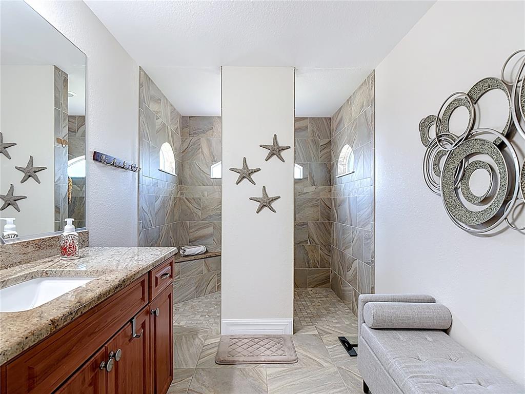 A bathroom features a wooden vanity, a walk-in shower with dual entries, and tile flooring — 70 CLUBHOUSE ROAD, ROTONDA WEST, FL