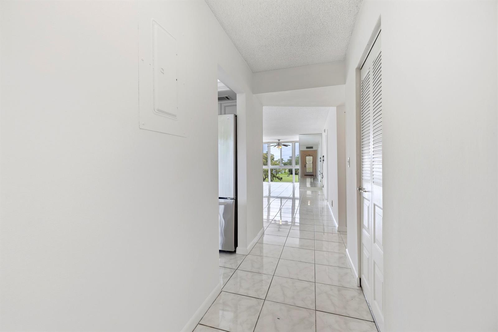 A bright hallway with white walls and light-colored tile flooring leads toward a distant window — 1480 NW 80th Avenue # 402, Margate FL 33063, MARGATE, FL