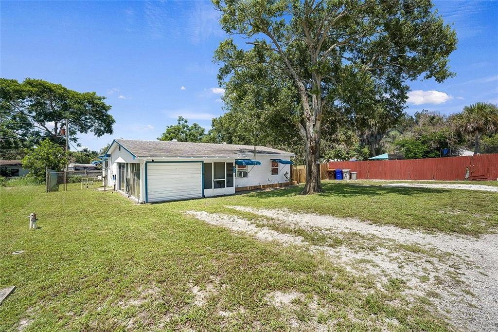 A white single-story house with a gravel driveway and a large tree in the yard — VERO BEACH, FL