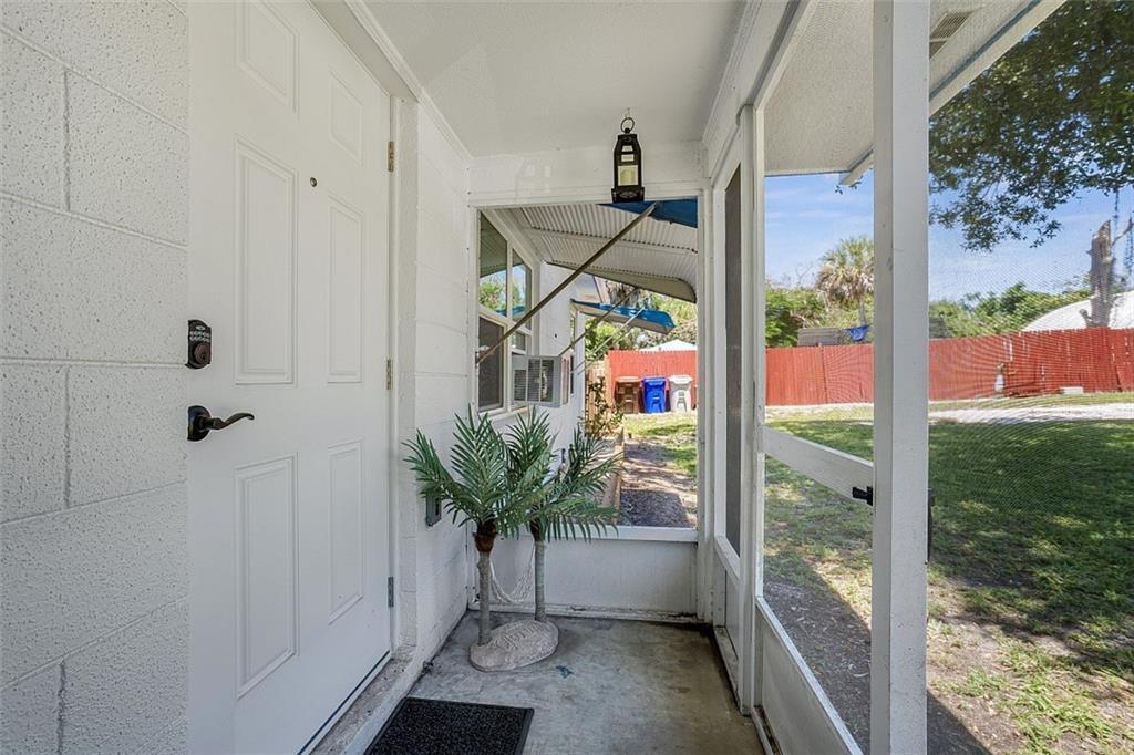 A white front door opens onto a screened-in porch with a concrete floor and palm decor — VERO BEACH, FL