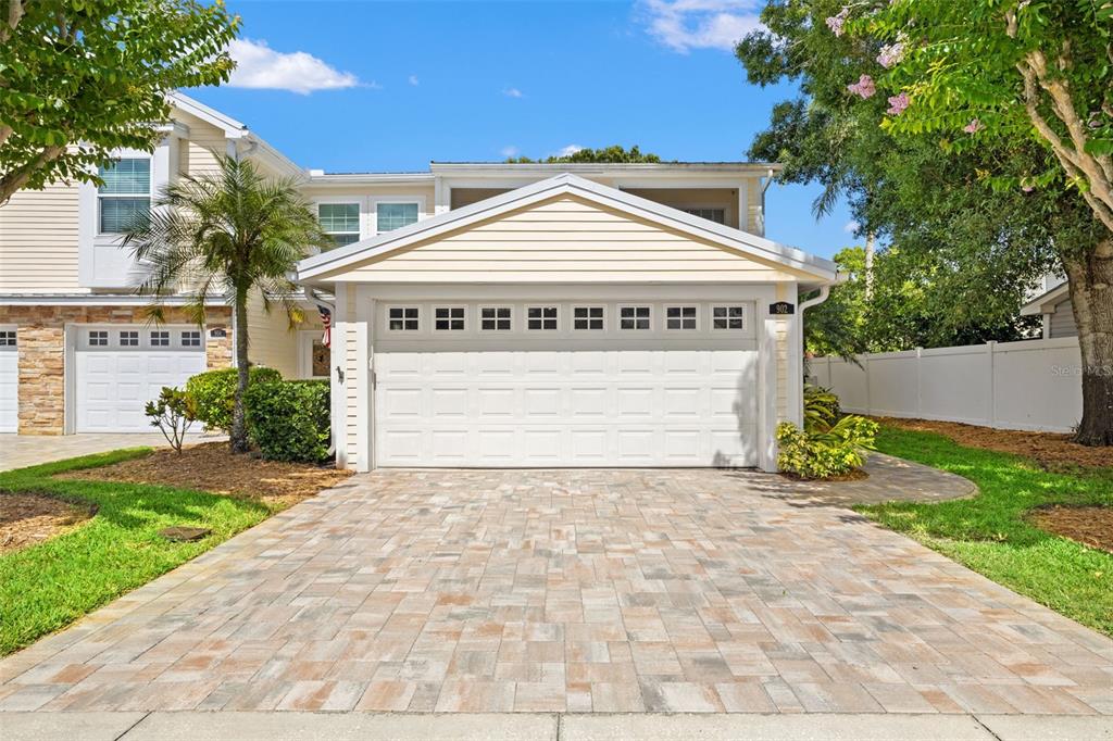 A two-story house exterior features a paved driveway, a white garage door, and landscaping — 902 WOODBRIDGE COURT, SAFETY HARBOR, FL
