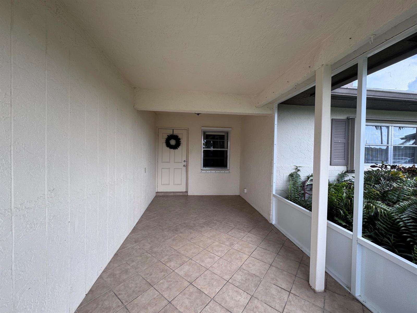A covered porch features tiled flooring, a white front door, and a screened-in side area — 6401 Lasalle Drive, Delray Beach FL 33484, DELRAY BEACH, FL